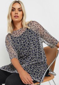 Transparent, let top med et blåt og sort leopardprint på en lys grå baggrund; har korte ærmer og en løs pasform.