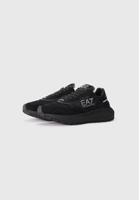 Zapatillas negras con parte superior de gamuza y malla, cuello acolchado, cordones, suela texturizada y detalles en plata con marca en el lateral y en la lengüeta.