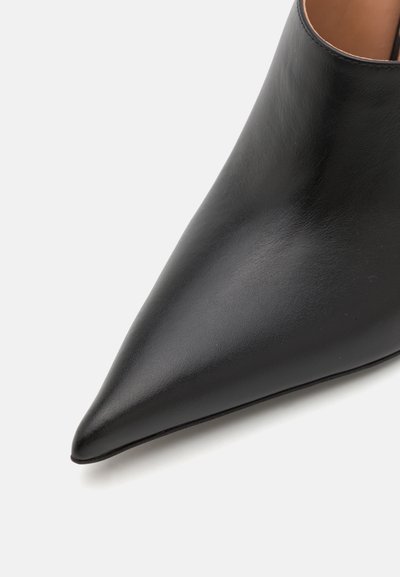 Musta nahkasaapas teräväkärkisellä muodolla, jossa on sileä pinta ja minimaalinen ommel, suunniteltu avointa takaa varten, jonka ansiosta se on helppo pukea.