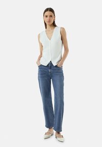 Weißes ärmelloses Top mit tiefem V-Ausschnitt und Knopfleiste vorne, kombiniert mit mittelblauen geraden Jeans und cremefarbenen spitzen Ballerinas.