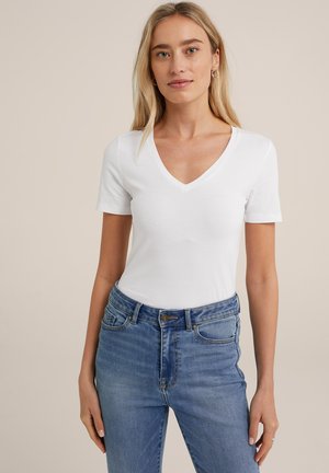 Conferință albă cu mâneci scurte în formă de V, fabricată din bumbac moale, asociată cu blugi din denim albastru, ajustați, cu talie medie și o ușoară decolorare.