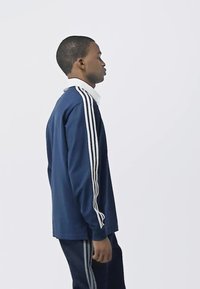 Navy long-sleeve crewneck top with three white stripes on each shoulder, paired with matching navy pants featuring stripe accents.