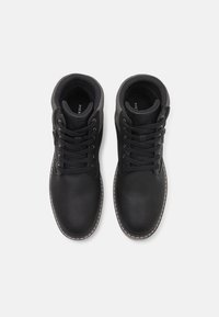 Botas de cuero negro hasta el tobillo con punta redonda, cuello acolchado, cierre con cordones en la parte delantera y cremallera lateral. Presentan un acabado texturizado y costuras en blanco contrastantes.