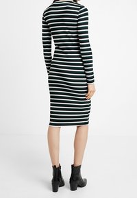 Langärmliges, geripptes Kleid mit vertikalen schwarz-weißen Streifen, figurbetonte Silhouette, knielanger Saum, kombiniert mit schwarzen Ankle-Boots.