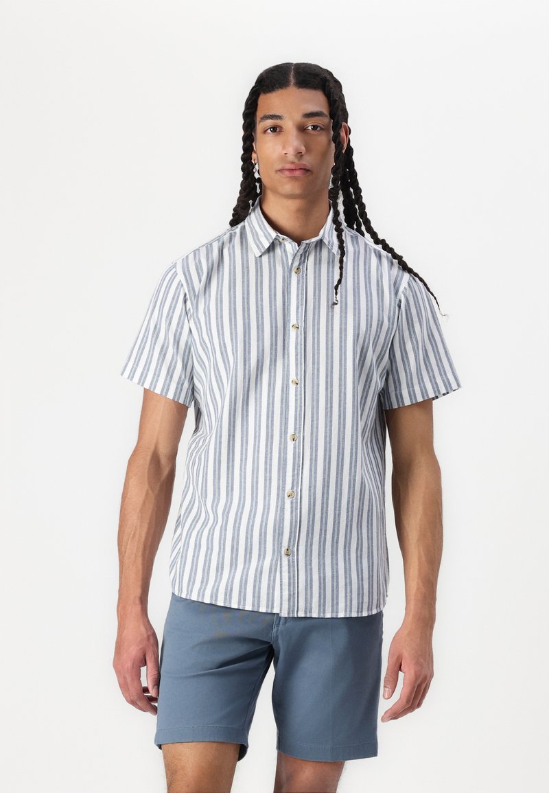 Chemise à manches courtes avec des rayures verticales bleues et blanches, un col classique et des boutons beiges, associée à un short bleu clair.