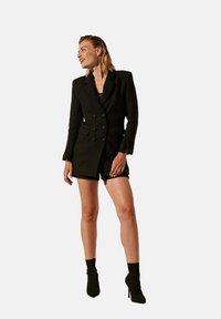 Blazer noir texturé à boutons croisés, porté sur un haut noir et un short, associé à des bottines noires montant à la cheville.
