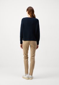 Suéter de malha canelada azul marinho, com corte descontraído, combinado com calças slim fit bege claro e ténis brancos, visto de costas.