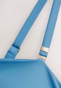 Blauer Rucksackriemen mit strukturierter Stoffoberfläche, Metallbeschlägen und verstellbaren Verschlüssen für einen sicheren Sitz.