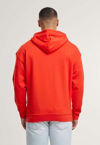 Felpa con cappuccio rossa caratterizzata da una vestibilità comoda, una texture morbida e polsini a costine, abbinata a jeans azzurri chiari. Design semplice, senza grafiche.