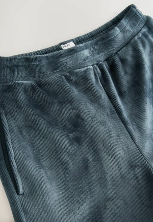 Sötét türkiz színű bolyhos sportnadrág, bordás textúrával, rugalmas derékkal és oldalsó zsebekkel. Márkajelzés a deréknál.