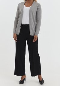 Světlé šedé kardigan s otevřeným předním dílem, žebrované okraje, nošený přes bílou košili a doplněný černými širokými kalhotami a černými lodičkami.