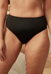 Crne bikinice s visokim strukom, izrađene od glatke tkanine, s elegantnim dizajnom i minimalnim detaljima za čist i moderan izgled.