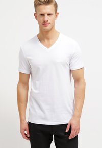 White cotton V-neck t-shirt with short sleeves, featuring a smooth texture and fitted design, displayed on a model against a light background.