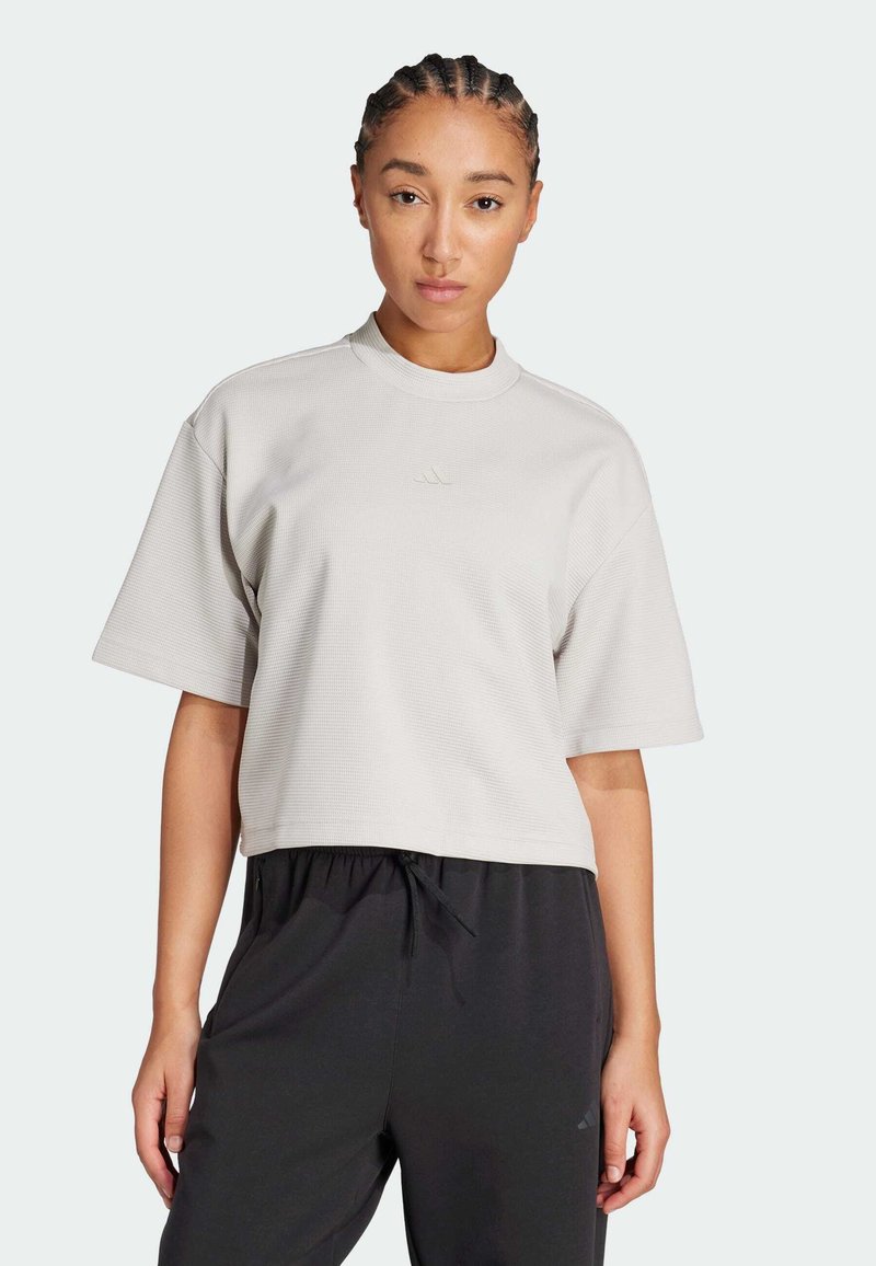 Camiseta corta de manga corta de color gris claro con textura acanalada y cuello redondo, con un logo sutil en el pecho.