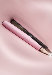 Rosa hårstylare med en elegant design, utrustad med en roséguldaccents och mörn keramikplåt, mot en slät rosa bakgrund.