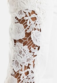 Hvidt stof med indviklet blomsterblondebroderi, der viser hud gennem openwork på et ærme.