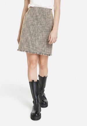Jupe en tweed tissé beige avec des éclats noirs, présentant un ourlet effiloché. Associée à de longues bottes en cuir noir avec une semelle épaisse et des fermetures éclairs.