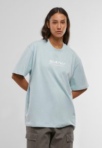 Gaiši zils kokvilnas T-krekls ar brīvu piegriezumu, īsām piedurknēm un apaļu kaklu. Uz priekšpuses ir balta uzdruka "KANI TheOriginator".