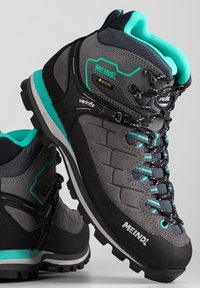 Grijze wandelschoenen met teal-accenten, voorzien van een gestructureerde bovenkant, stevige veters en een robuuste buitenzool. Gemarkeerd met "Meindl" en "Gore-Tex."