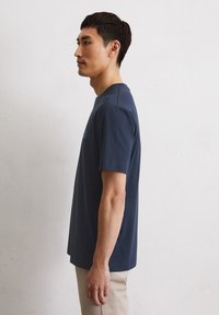 Marineblaue Baumwoll-T-Shirt mit Rundhalsausschnitt, kurzen Ärmeln und lässiger Passform, gezeigt auf einer Person im Profil vor einem schlichten Hintergrund.