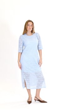 Vrouw draagt een lichtblauwe midi-jurk van kant met ellebooglange mouwen en een zoomsplit, gecombineerd met bruine, puntige lage hakken met slingback.