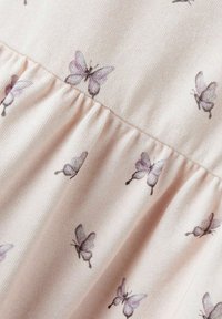 Vaaleanpunainen kangas, jossa on pehmeä rakenne, esittelee pienen, herkän violetin perhosen kuvion ja muotoa antavan kerrotemerkin.