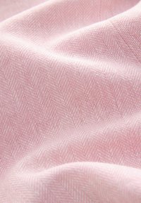 Tessuto rosa tenue con un delicato motivo a spina di pesce, che mostra pieghe morbide e dettagli della texture.
