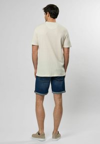 Hvit teksturert kortermet t-skjorte kombinert med blå denimshorts, med rullede ermer og diskret baklomme-detalj. Lette fottøy.