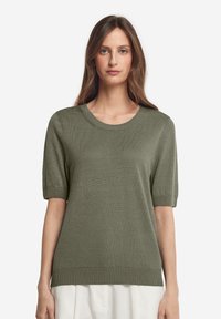 Olivgrön kortärmad stickad tröja med rund halsringning, mjuk textur och ribbad nederkant, med en avslappnad passform.