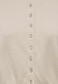 Geknöpfter Cardigan in Hellbeige mit gerippter Textur, sieben runde, glatte Knöpfe mit leichtem Glanz entlang der Vorderseite.