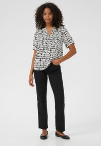 Blouse noire et blanche à manches courtes avec un motif à pois, associée à un pantalon noir à jambe droite et des chaussures plates noires.
