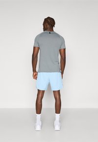 Gray short-sleeve shirt with a black label at the back, paired with light blue textured shorts. White sneakers and socks complete the look.