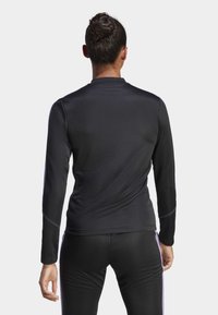 Maglietta atletica nera a maniche lunghe con una texture liscia, caratterizzata da cuciture viola a contrasto lungo le spalle e i lati.