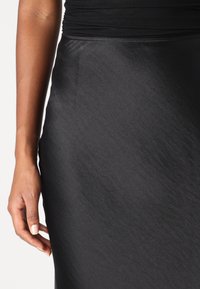 Gros plan sur la main d'une personne reposant à côté d'une jupe en satin noir lisse et d'un haut noir ajusté avec des détails froncés.