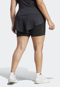 Černé sportovní šortky s vrstevnatým designem, vysokým pasem a hladkou texturou. Kombinované s bílými sportovními botami.