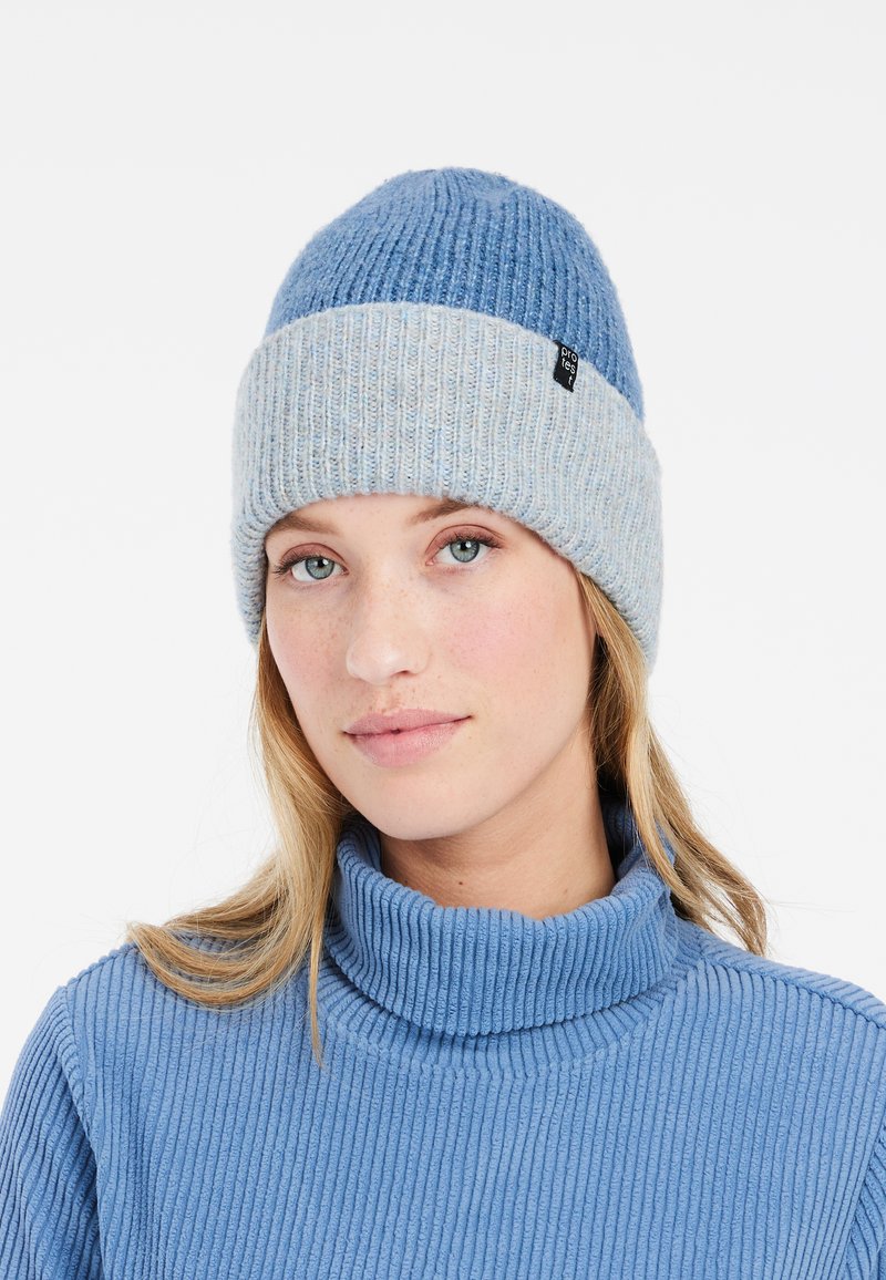Bonnet tricoté en bleu clair et bleu foncé, avec une texture côtelée et un revers replié. Comprend une petite étiquette noire sur le côté.