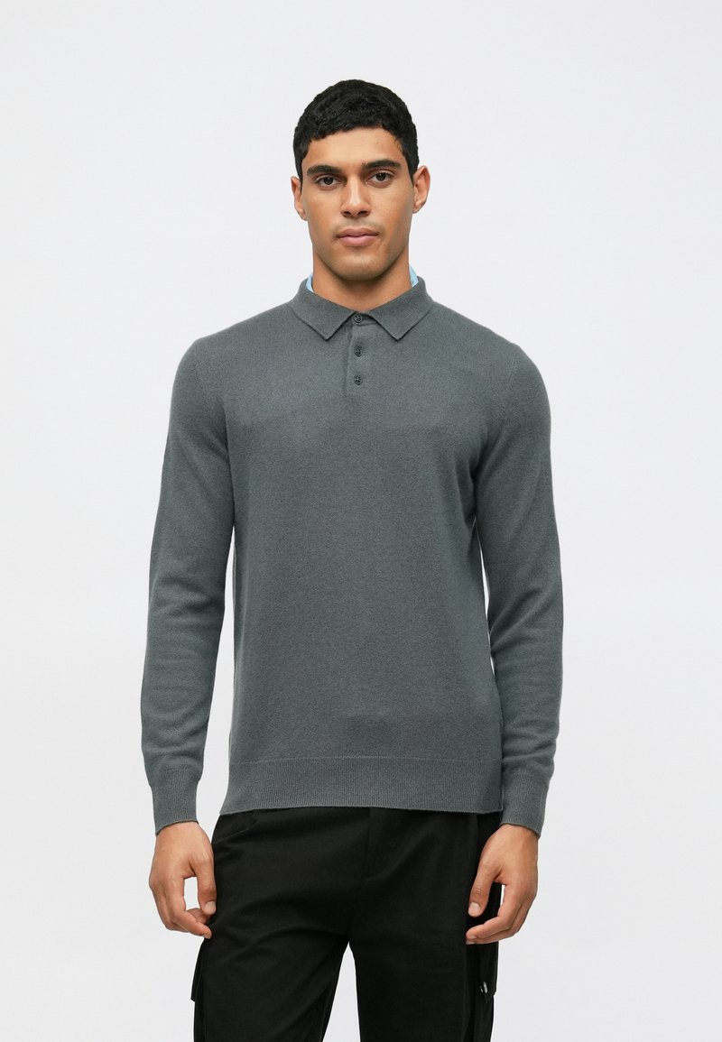 Gray long-sleeve polo sweater with a collar and three buttons. Features a fine knit texture and a ribbed hem, paired with dark pants.