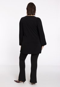 Tunique noire à côtes avec de longues manches bouffantes, associée à un pantalon noir ajusté. La tunique a une coupe décontractée et un décolleté en forme deU.