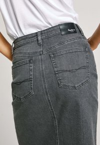 Siva denim krilo z oprijetim krojem, ki vsebuje dve zadnji žepki in črno usnjeno oznako na pasu. Teksturirana tkanina z detajli šivanja.