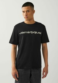 T-shirt nera in cotone con il logo "jamiroquai" in crema, maniche corte, collo rotondo e vestibilità rilassata. Design semplice senza ulteriori pattern.