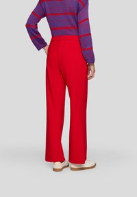 Red wide-leg trousers with a smooth texture, elastic waistband, and paired with white sneakers. The background is neutral gray.