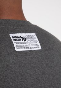 Graues Baumwoll-Polyester-Gemischhemd mit einem Etikett, auf dem "GORILLA WEAR" steht, das Pflegehinweise und das Ursprungsland auf der Rückseite sichtbar zeigt.