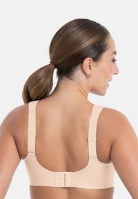 Beżowy bezprzewodowy biustonosz z regulowanymi ramiączkami, gładkim materiałem oraz zapięciem na haftki z tyłu. Posiada niskie wycięcie dla komfortu.