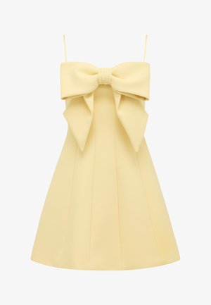 Rihmadeta helekollane kleit suure dekoratiivse paelaga rinnaosas ja keha järgiva ülaosaga, mis voolab A-lõikeline seelikusse.