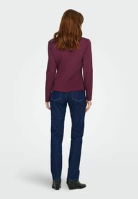 Bordeaux lange mouwen top met een aansluitend ontwerp, gecombineerd met donkere blauw rechte jeans. Zwarte enkellaarsjes maken de outfit af.