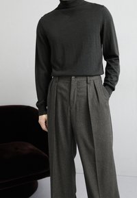 Ciemny golf i wysokiej talii plisowane szare spodnie. Gładka faktura; sweter ma prążkowany kołnierz i dopasowane rękawy.