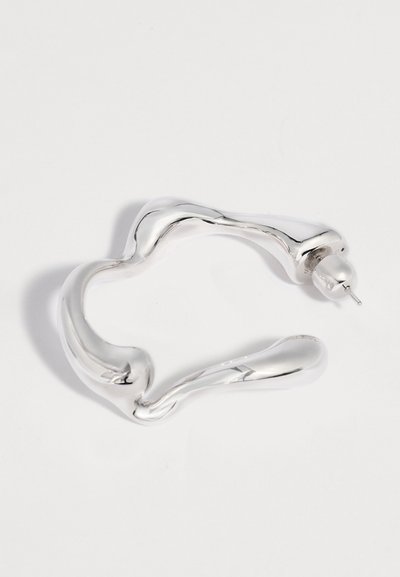 Ασημένιου τόνου σκουλαρίκι σε σχήμα κύκλου με αφηρημένες, ομαλές και ακανόνιστες καμπύλες και πίσω κούμπωμα με καρφί, σε λευκό φόντο.