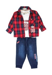 Chemise à carreaux rouge et bleu boutonnée superposée à un t-shirt blanc avec un graphique. Associée à un pantalon en denim bleu foncé avec une étiquette d'accent.