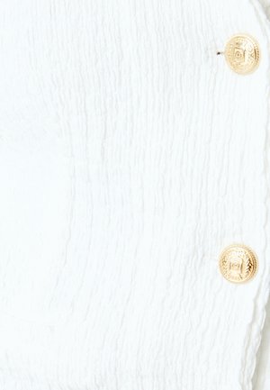 Tessuto bianco testurizzato con un motivo rigato, dotato di due bottoni dorati con un design decorativo per la chiusura.