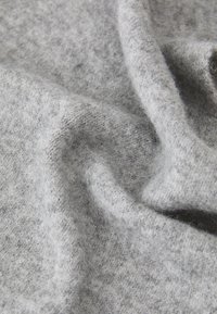 Tela gris con una textura suave y esponjosa, que presenta un tejido sutil y desigual. El material parece ligero y se drapea con suavidad.